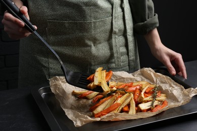 Photo of Cooker near baking pan with tasty parsnip and bell pepper at dark grey table, closeup
