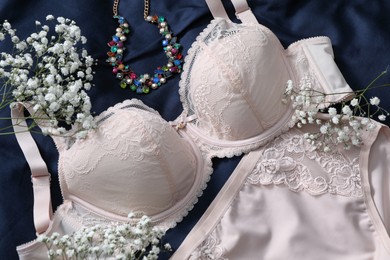 Elegant plus size women's underwear, gypsophila flowers and necklace on dark blue fabric, closeup