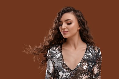 Photo of Beautiful young woman with long curly hair in sequin dress on brown background, space for text