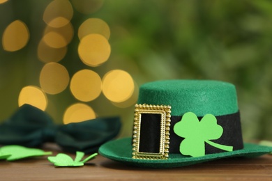 Leprechaun hat and clover leaves on wooden table against blurred lights, space for text. St Patrick's Day celebration