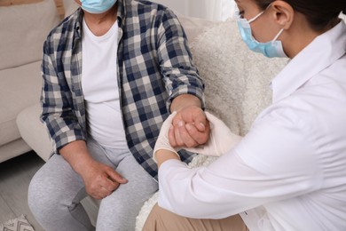 Photo of Doctor in protective mask checking pulse of senior man at nursing home, closeup