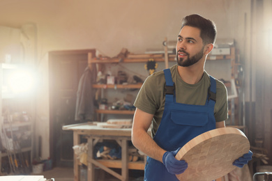 Photo of Professional carpenter with round piece of wood in workshop