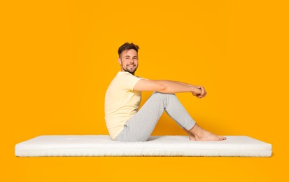 Photo of Smiling man posing on soft mattress against orange background