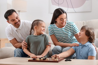 Photo of Parents playing checkers with children at table in room