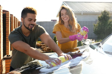Happy young couple washing car at backyard on sunny day