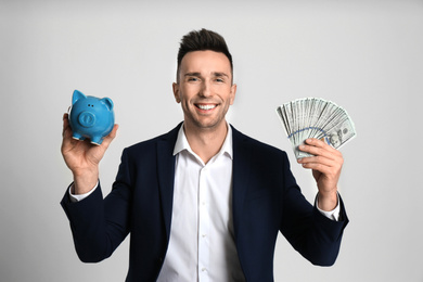 Happy man with cash money and piggybank on light grey background