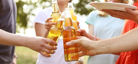 Friends with bottles of beer and food outdoors, closeup. Banner design
