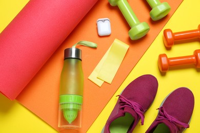 Photo of Exercise mat, dumbbells, bottle of water, wireless earphones, fitness elastic band and shoes on yellow background, flat lay