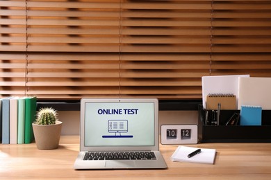Laptop with online test on wooden desk in office