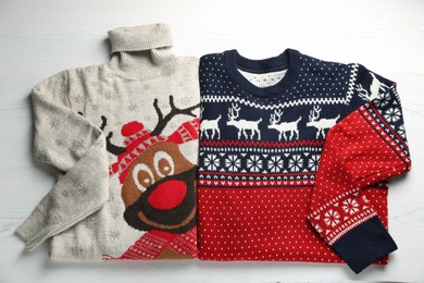 Photo of Warm Christmas sweaters on white wooden table, top view