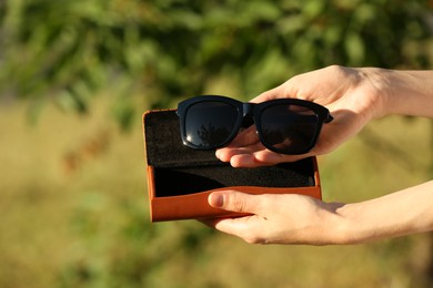 Photo of Woman holding sunglasses and case outdoors on sunny day, closeup
