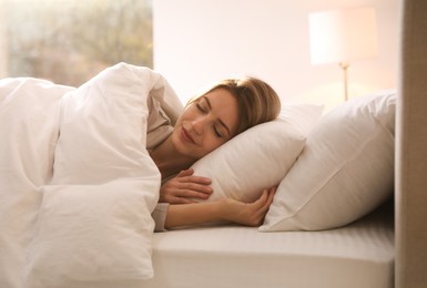 Woman under warm white blanket sleeping in bed indoors
