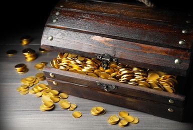 Open treasure chest with gold coins on grey wooden table, closeup 