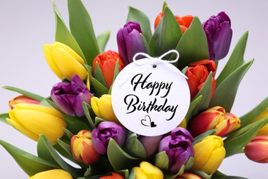 Image of Beautiful bouquet of tulip flowers with Happy Birthday card on light background, closeup
