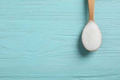 Photo of Spoon of white sugar on light blue wooden table, top view. Space for text