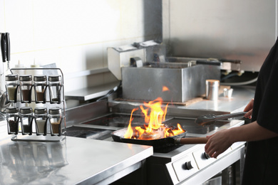 Female chef cooking meat with burning flame on stove in restaurant kitchen, closeup