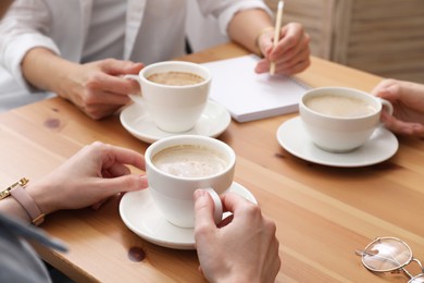 Women with cups of coffee at table in cafe, closeup