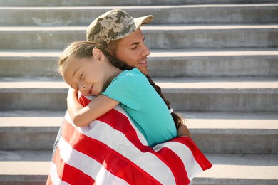 Soldier with flag of USA and his little daughter hugging outdoors, space for text