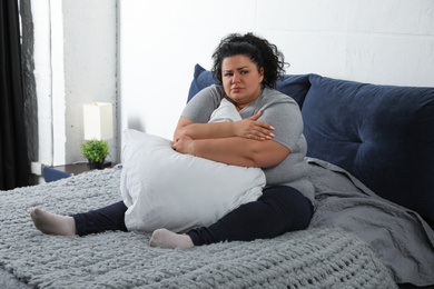 Depressed overweight woman hugging pillow on bed