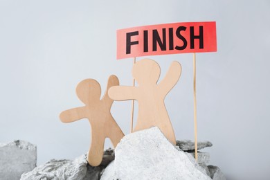 Competition concept. Wooden human figures on stones and red sign with word Finish against grey background