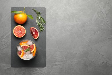 Delicious refreshing drink with sicilian orange and rosemary near fresh ingredients on grey table, flat lay. Space for text