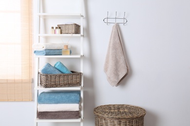 Shelving unit and rack with clean towels and toiletries near white wall