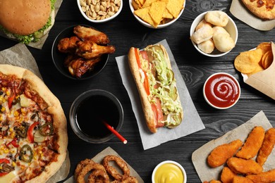Photo of Chicken wings, onion rings and other fast food on black wooden table, flat lay