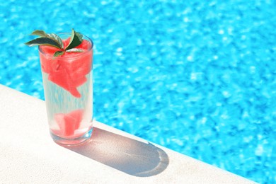 Refreshing watermelon drink in glass near swimming pool outdoors. Space for text