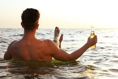 Photo of Young man with drink on inflatable ring in sea, back view