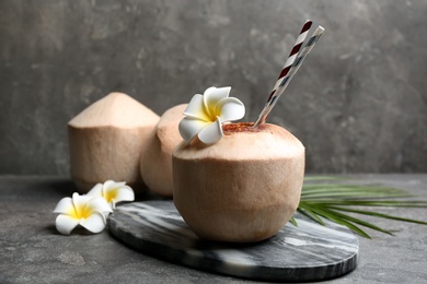 Young peeled coconuts with straw, palm leaf and beautiful flowers on grey table