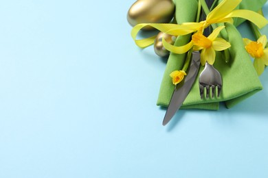 Photo of Cutlery set, Easter eggs and narcissuses on light blue background, space for text. Festive table setting