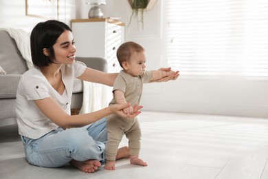 Mother supporting her baby daughter while she learning to walk at home. Space for text