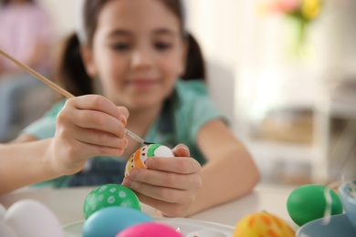Little girl painting Easter eggs at table indoors, focus on hands