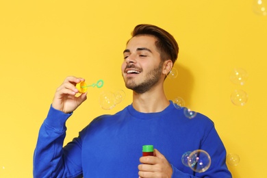 Photo of Young man blowing soap bubbles on color background