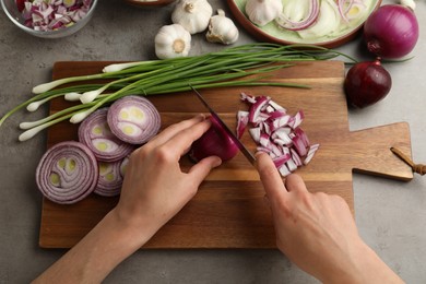 Photo of Woman cutting red onion on wooden board at grey table, above view