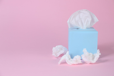 Box with paper tissues and used crumpled napkins on pink background, space for text
