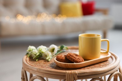 Yellow mug, cookies and eustoma flowers on rattan table in living room
