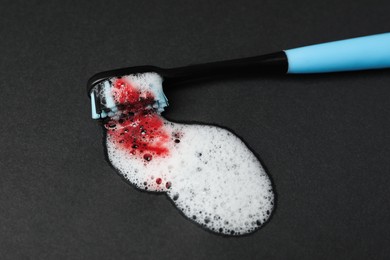 Photo of Toothbrush with paste and blood on black background, closeup. Gum inflammation