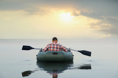 Man rowing inflatable rubber fishing boat on river, back view