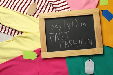 Photo of Small chalkboard with phrase SAY NO TO FAST FASHION and different clothes, top view