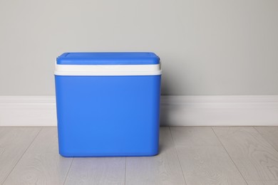 Closed blue plastic cool box near light grey wall indoors. Space for text