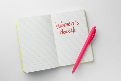 Notebook with words Women's Health and pen on white background, top view