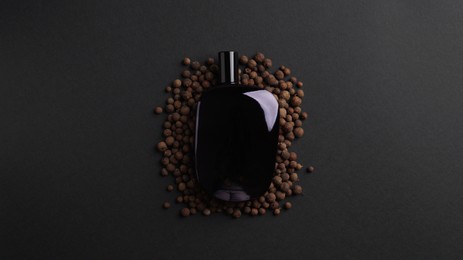 Bottle of perfume surrounded by allspice on dark background, top view