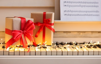 Gift boxes and fairy lights on piano keys, closeup. Christmas music