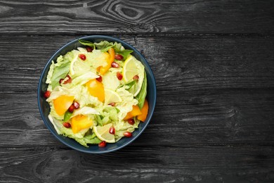 Delicious salad with Chinese cabbage, lemon, persimmon and pomegranate seeds on black wooden table, top view. Space for text