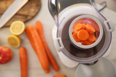 Modern juicer with fresh slices of carrot on table, top view