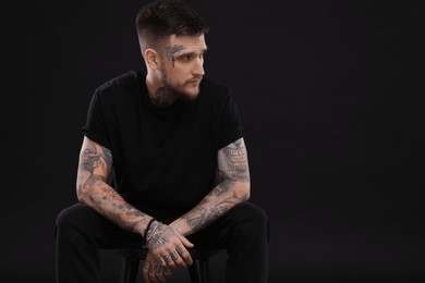 Photo of Handsome hipster man sitting on chair against black background. Space for text