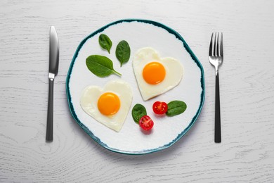 Photo of Heart shaped fried eggs served on white wooden table, flat lay