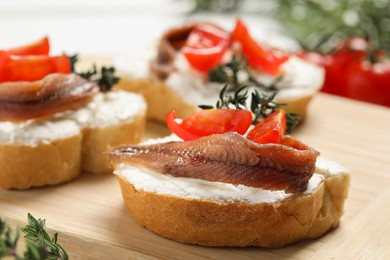 Photo of Delicious sandwiches with cream cheese, anchovies and tomatoes on wooden board, closeup