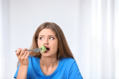 Portrait of unhappy woman eating broccoli on light background